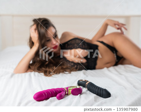 A beautiful woman in lingerie lies on a bed and chooses a vibrator. A beautiful woman in lingerie lies on a bed and chooses a vibrator. 135907980