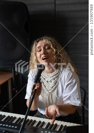 Caucasian woman singing into microphone and playing synthesizer and recording herself on laptop.  135907989