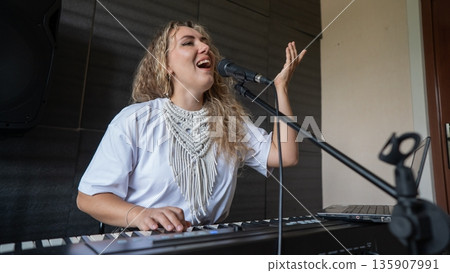 Caucasian woman singing into microphone and playing synthesizer and recording herself on laptop.  135907991