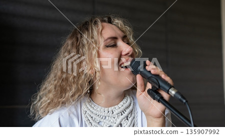 Caucasian woman singing into microphone in music studio. Caucasian woman singing into microphone in music studio. 135907992