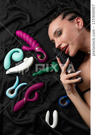 Portrait of Caucasian woman lying on bed among sex toys.  135908007