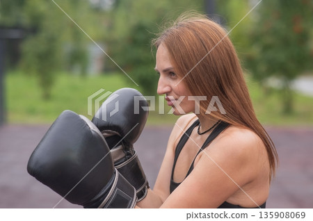 A Caucasian woman practices boxing outdoors.  135908069