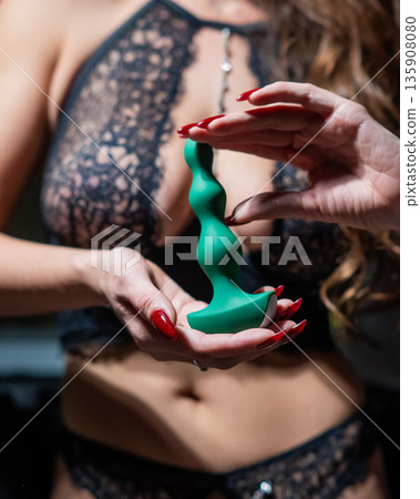 Woman in lace lingerie holding green anal beads.  135908080