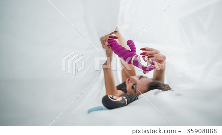 Woman in lace lingerie holds a dildo. A beautiful Caucasian woman lies under the sheets and holds a dildo. Woman in lace lingerie holds a dildo. A beautiful Caucasian woman lies under the sheets and holds a dildo. 135908088