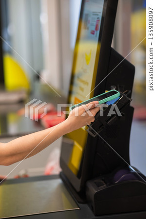 A woman pays using her smartphone at a self-checkout.  135908097