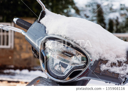 Close up of a scooter headlight and handlebars covered in fresh snow, outdoors in winter. 135908116