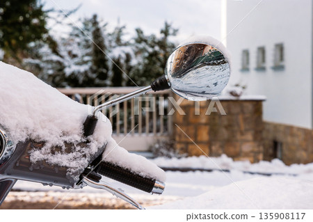 Snow covered scooter handlebar and mirror parked on the city street in winter Snow covered scooter handlebar and mirror parked on the city street in winter 135908117