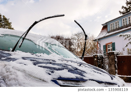 Snow covered car windshield with raised wiper blades, parked in residential street 135908119