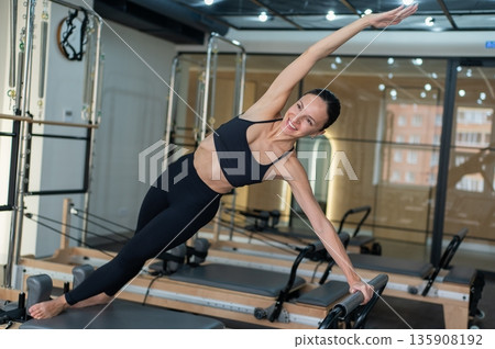 Caucasian woman doing side bends on reformer machine. Caucasian woman doing side bends on reformer machine. 135908192