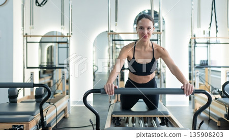 Caucasian woman doing exercises on reformer machine.  135908203