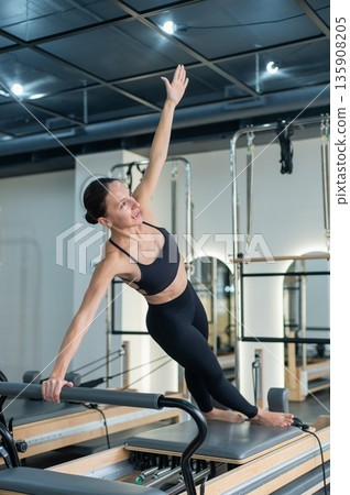 Caucasian woman doing side bends on reformer machine. Caucasian woman doing side bends on reformer machine. 135908205
