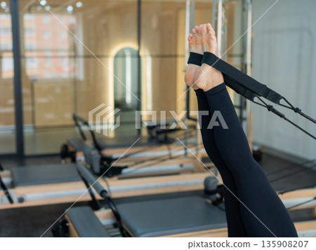 Caucasian woman doing exercises on reformer machine. Caucasian woman doing exercises on reformer machine. 135908207