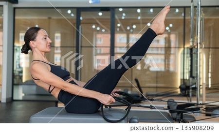 Caucasian woman doing exercises on reformer machine.  135908209