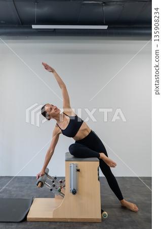 Caucasian woman doing Pilates on classic chair. Caucasian woman doing Pilates on classic chair. 135908234