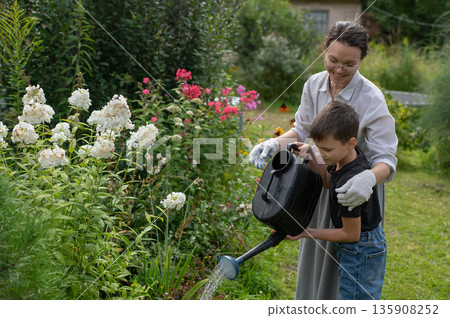 Caucasian woman and her son watering flowers in the garden. Caucasian woman and her son watering flowers in the garden. 135908252