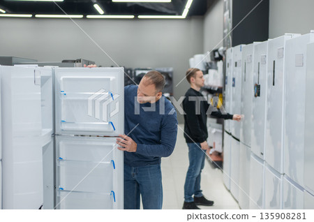 Two Caucasian men are choosing a refrigerator in a hardware store. Two Caucasian men are choosing a refrigerator in a hardware store. 135908281