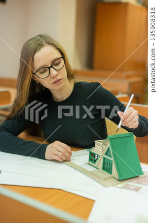 Caucasian young woman making a model of a building. Student of the construction university. Caucasian young woman making a model of a building. Student of the construction university. 135908318