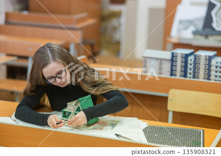 Caucasian young woman making a model of a building. Student of the construction university.  135908321