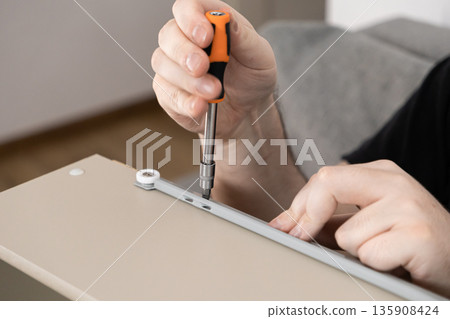 Man's hands carefully using a screwdriver to install a drawer runner on furniture, representing home improvement, assembly, and DIY projects Man's hands carefully using a screwdriver to install a drawer runner on furniture, representing home improvement, assembly, and DIY projects 135908424