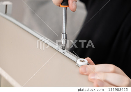 A person's hands precisely assemble modern furniture, using a screwdriver to attach a sliding drawer mechanism, symbolizing practical home improvement and DIY skill 135908425
