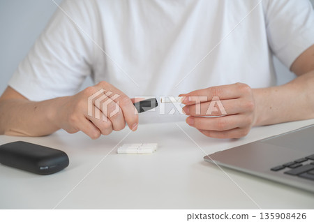 A woman smokes an electronic cigarette while working on a laptop. Tobacco heating system. A woman smokes an electronic cigarette while working on a laptop. Tobacco heating system. 135908426