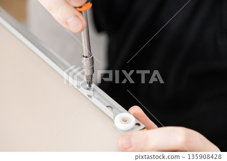 A person's hands expertly using a screwdriver to fasten a screw into a metal furniture rail, showcasing precise assembly, DIY construction, and dedicated home improvement work A person's hands expertly using a screwdriver to fasten a screw into a metal furniture rail, showcasing precise assembly, DIY construction, and dedicated home improvement work 135908428