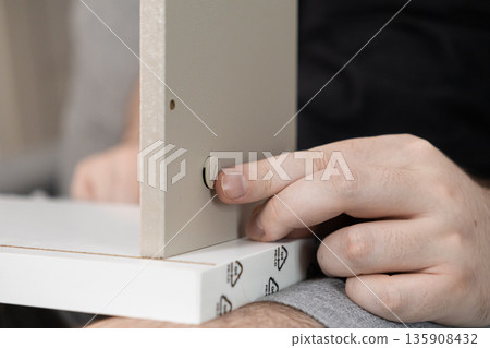 Person's hand assembling flat-pack furniture, inserting a plastic fastener into a wooden board, symbolizing practical DIY home improvement and construction Person's hand assembling flat-pack furniture, inserting a plastic fastener into a wooden board, symbolizing practical DIY home improvement and construction 135908432
