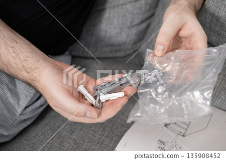 Person's hands organizing small furniture assembly hardware, including screws and wall plugs, with an instruction manual, for home DIY project 135908452