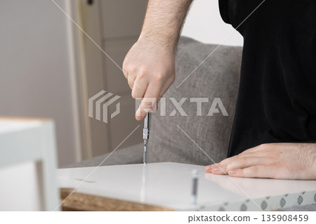 Close-up of a person assembling white furniture with a screwdriver, representing dedication to home improvement, craftsmanship, and DIY projects 135908459