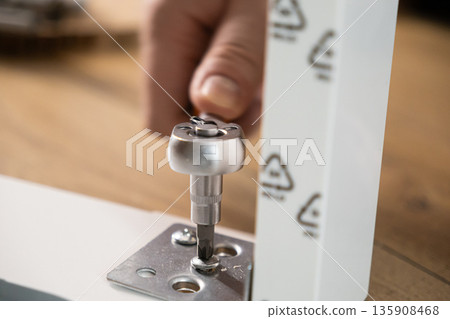 Close-up of a hand using a ratchet screwdriver to secure a screw into a metal bracket, representing DIY furniture assembly and home improvement projects 135908468