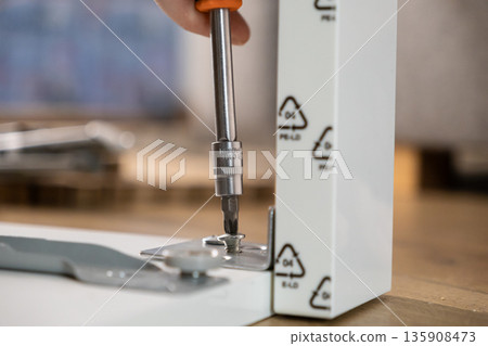 Hand using a screwdriver to assemble white furniture panel with a metal bracket, highlighting DIY home improvement and the importance of PE-LD plastic recycling Hand using a screwdriver to assemble white furniture panel with a metal bracket, highlighting DIY home improvement and the importance of PE-LD plastic recycling 135908473