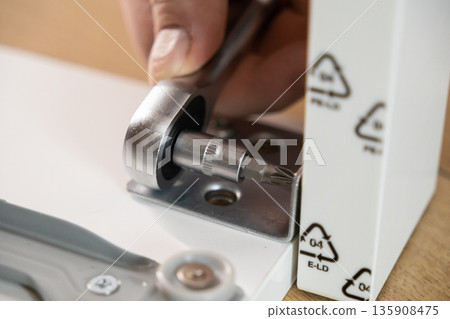A person's hand meticulously using a ratchet wrench with a Torx bit, precisely tightening a screw into a metal bracket for efficient home furniture assembly 135908475