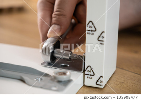 Person's hand using a ratchet wrench for furniture assembly, tightening a screw on a white component, symbolizing practical DIY skills and home construction 135908477
