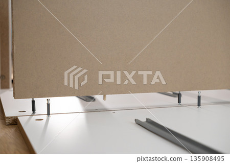 Assembling flat-pack furniture components, revealing detailed connections with dowel pins and cam lock fittings for a home improvement project Assembling flat-pack furniture components, revealing detailed connections with dowel pins and cam lock fittings for a home improvement project 135908495