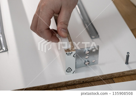 Hand inserting a white plastic dowel into particle board, symbolizing practical home improvement, furniture assembly, and a successful DIY construction project 135908508