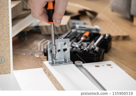 Close-up of a hand using a screwdriver to fasten a metal bracket onto wooden furniture, symbolizing practical DIY home assembly and essential repair work Close-up of a hand using a screwdriver to fasten a metal bracket onto wooden furniture, symbolizing practical DIY home assembly and essential repair work 135908519