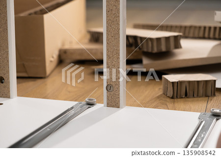 Close-up of flat-pack furniture assembly in progress on a wooden floor, emphasizing the DIY process for home improvement and modern interior setup 135908542