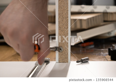 Person's hand assembling new furniture, tightening a screw into a white particle board panel, showcasing home improvement and successful DIY craftsmanship 135908544