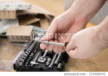 Hands selecting a versatile screwdriver from a comprehensive toolkit, preparing for furniture assembly, symbolizing practical DIY home improvement 135908545