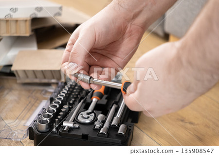 Man's hands assembling a versatile metal screwdriver from a comprehensive tool kit, illustrating readiness for DIY projects and intricate home repair tasks Man's hands assembling a versatile metal screwdriver from a comprehensive tool kit, illustrating readiness for DIY projects and intricate home repair tasks 135908547