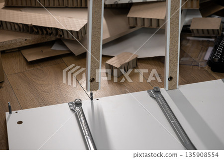 Assembly of white particle board furniture with a screw connection on a wooden floor, representing home improvement, DIY project, and flat-pack furniture construction process 135908554
