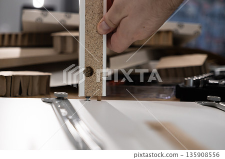 A person's hand precisely assembling furniture components, fitting a wooden panel with dowels and screws for a modern DIY home improvement project, highlighting construction A person's hand precisely assembling furniture components, fitting a wooden panel with dowels and screws for a modern DIY home improvement project, highlighting construction 135908556