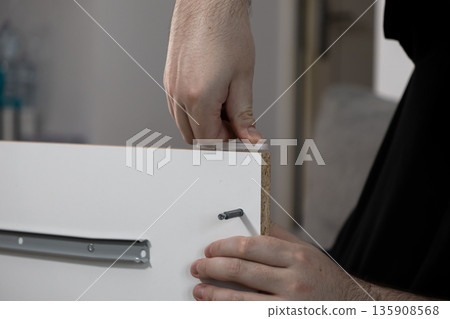 Person's hands expertly assembling white flat-pack furniture, installing a drawer slide during a home improvement or DIY construction project Person's hands expertly assembling white flat-pack furniture, installing a drawer slide during a home improvement or DIY construction project 135908568