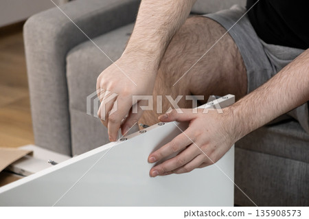 Male hands meticulously assembling modern white flat-pack furniture at home, symbolizing do-it-yourself efforts, new home setup, and personal achievement Male hands meticulously assembling modern white flat-pack furniture at home, symbolizing do-it-yourself efforts, new home setup, and personal achievement 135908573