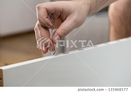 Person's hand carefully peeling protective film with recycling symbols from a new white furniture board during assembly, highlighting sustainability and home improvement 135908577