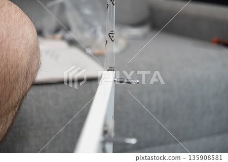 White furniture panel being assembled with a metallic dowel and screw connector, highlighting DIY home improvement in a domestic setting 135908581