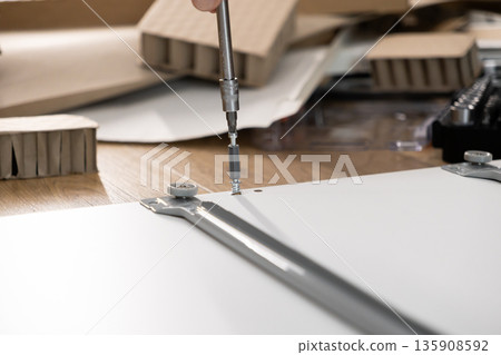 Person's hand assembling flat-pack furniture, carefully tightening a screw into a white board, illustrating home improvement, DIY, and self-assembly project concept Person's hand assembling flat-pack furniture, carefully tightening a screw into a white board, illustrating home improvement, DIY, and self-assembly project concept 135908592