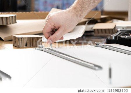 A person's hand carefully screws a metal bolt into a white furniture panel, illustrating the process of DIY assembly for home improvement projects A person's hand carefully screws a metal bolt into a white furniture panel, illustrating the process of DIY assembly for home improvement projects 135908593