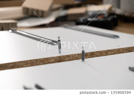 White chipboard panel with partially inserted cam lock fittings, representing flat-pack furniture assembly, DIY home improvement and construction White chipboard panel with partially inserted cam lock fittings, representing flat-pack furniture assembly, DIY home improvement and construction 135908594