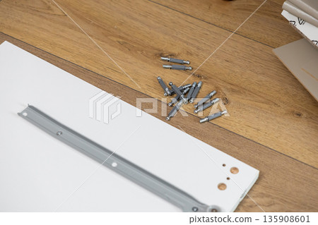 Modern white furniture panel, metal drawer slide, and a pile of cam dowels on wooden floor, symbolizing home improvement and easy DIY furniture assembly Modern white furniture panel, metal drawer slide, and a pile of cam dowels on wooden floor, symbolizing home improvement and easy DIY furniture assembly 135908601